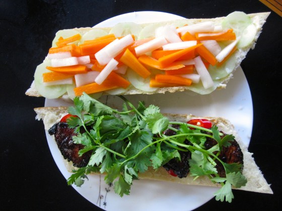 Assembled bánh mì - mayonnaise, cucumber and pickled vegetables on one side, mayonnaise, chili peppers, pork, and cilantro on the other